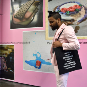 Photo of a young black man wearing a pink suit and a black tote bag against a pink wall