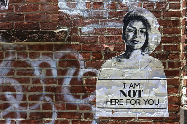Photo of woman on a brick wall with graffiti saying "I am not here for you"