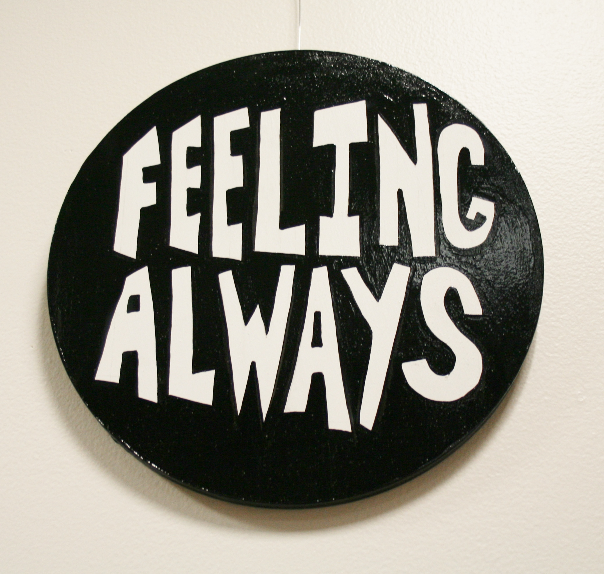 Round wall work reading, "Feeling always." in white letters against a black background