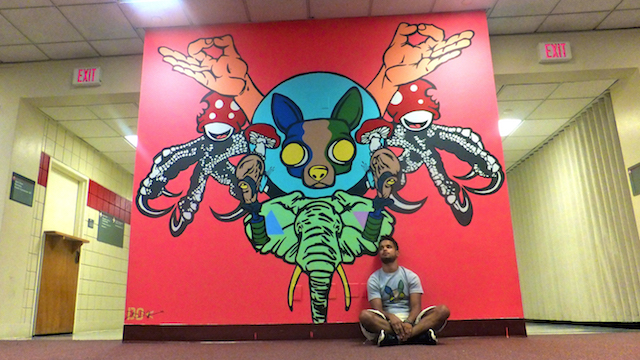 A young man sitting in front of a wall mural