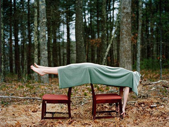Body lying across two chairs, draped in a green blanket, in a woodland setting