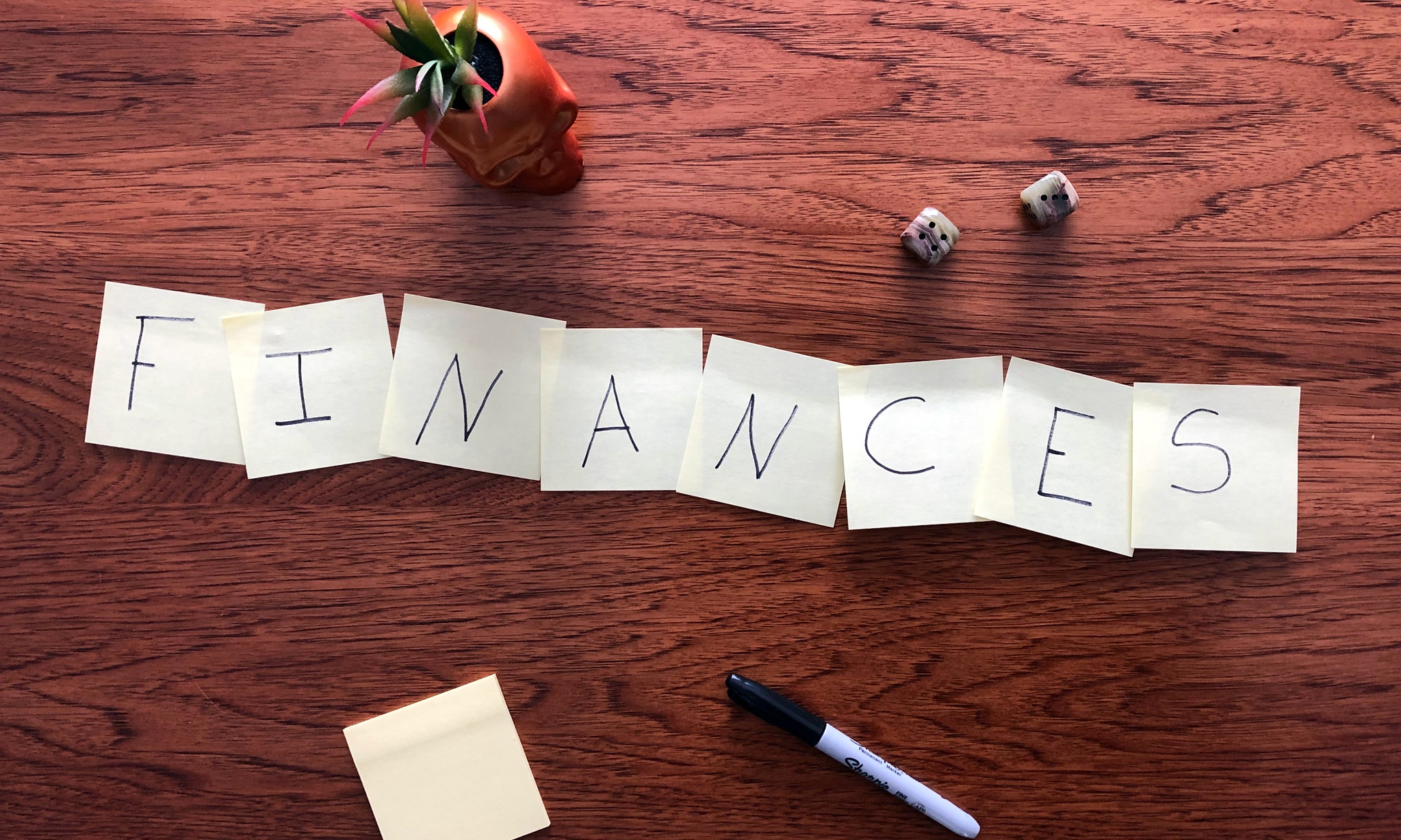 A wood desk with Post-It notes spelling out the word, "finances."