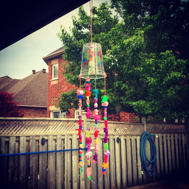 Plastic cup hanging from a ledge with colorful beads and string in resemblance of a wind chime.
