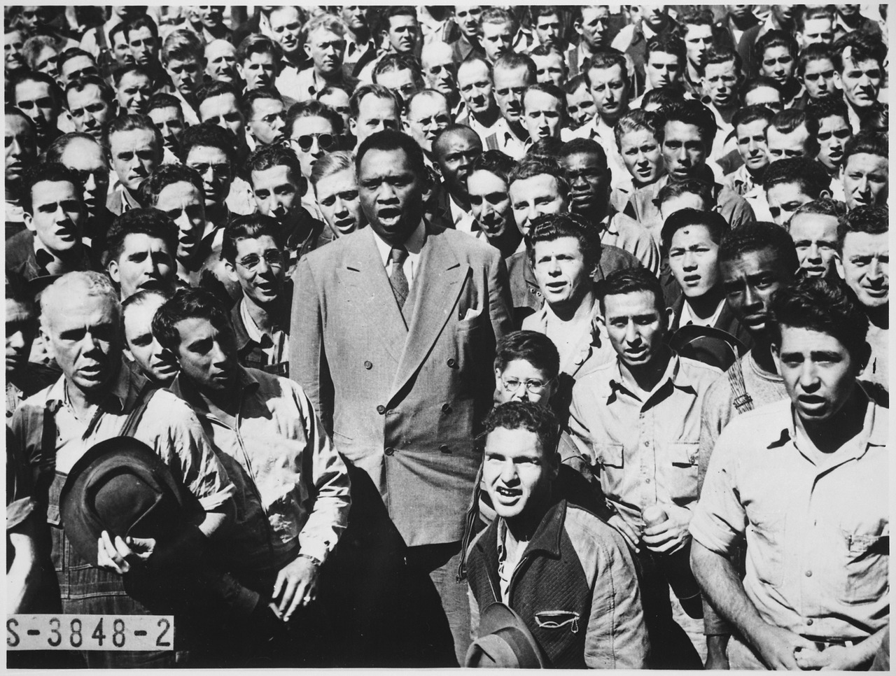 A Black man stands in the middle of a crowd, leading it in song