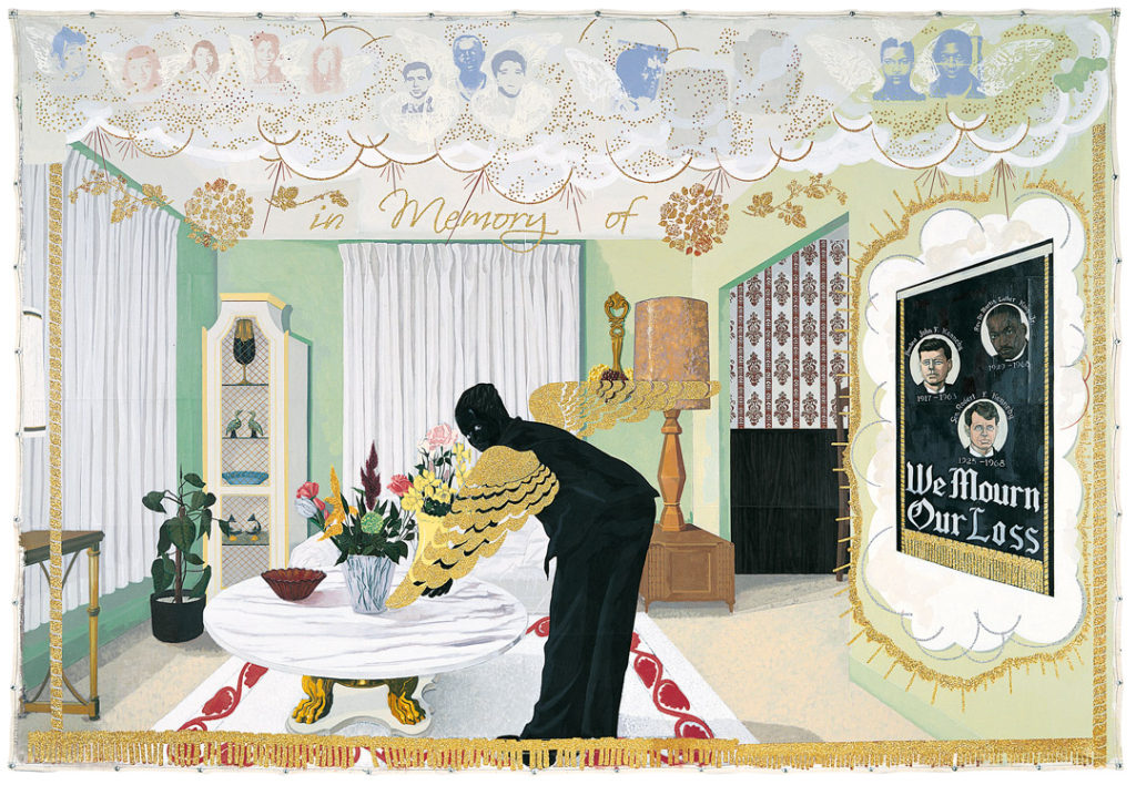 A Black figure with gold wings in a living room like setting bends over a table. Notably, there is a poster on the wall commemorating the lives of JFK, RFK, and Dr. Martin Luther King, Jr.